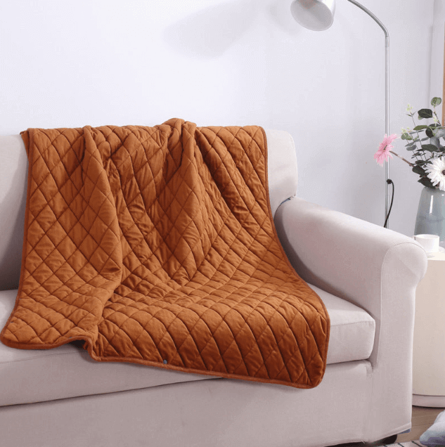 Toffee Ember heated blanket draped over a white sofa with quilted pattern
