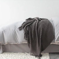 Dark Gray textured blanket draped over a bed with light gray bedding.