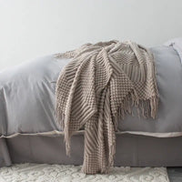 Beige knitted blanket with tassels on a gray bed