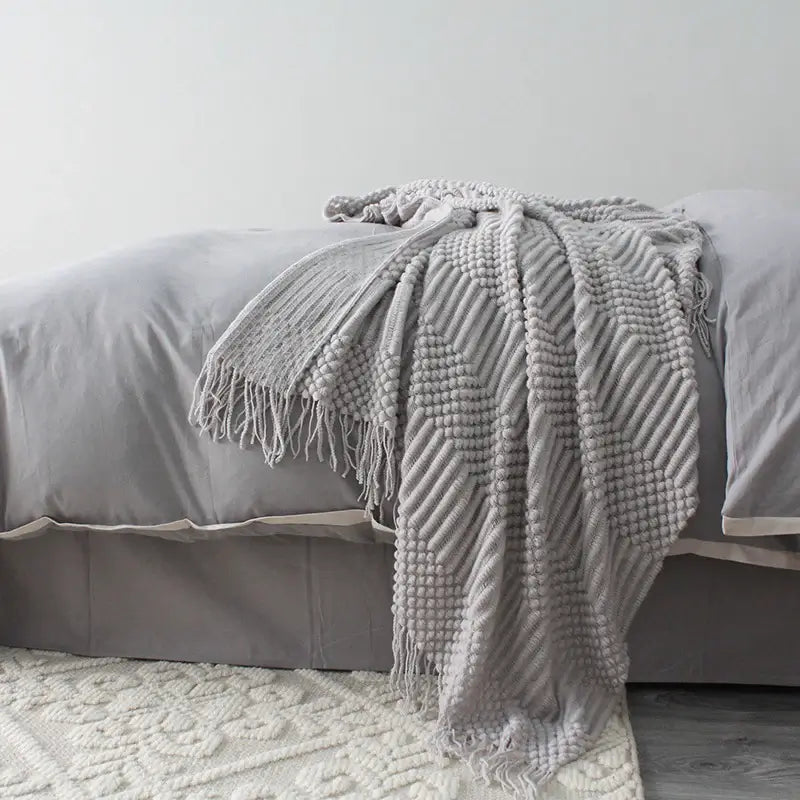Gray textured blanket draped over a bed with a light gray wall in the background