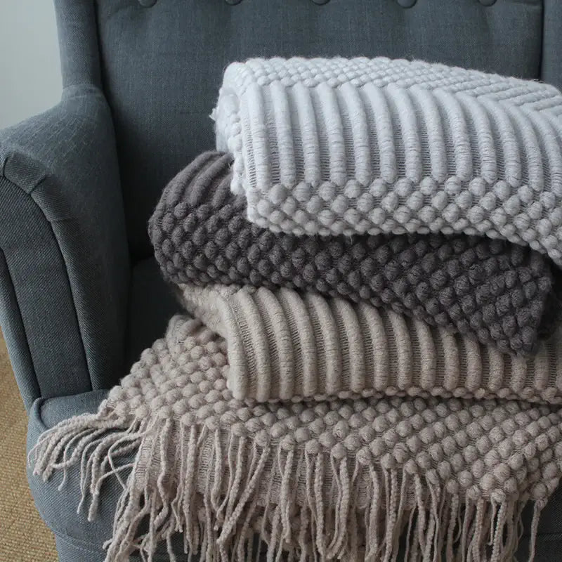 Dark grey plush nap blanket rolled on a chair with striped cushion